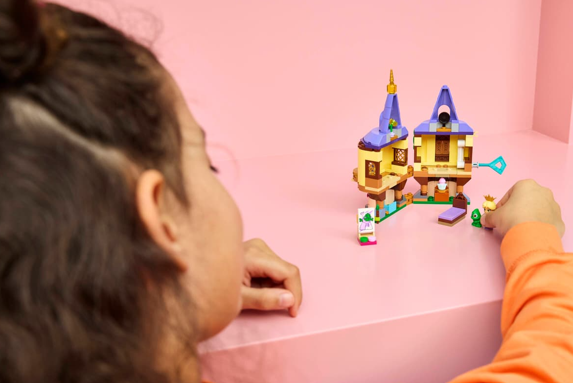 Kind spielt mit einem gelben und lila Lego-Schloss vor rosa Hintergrund.