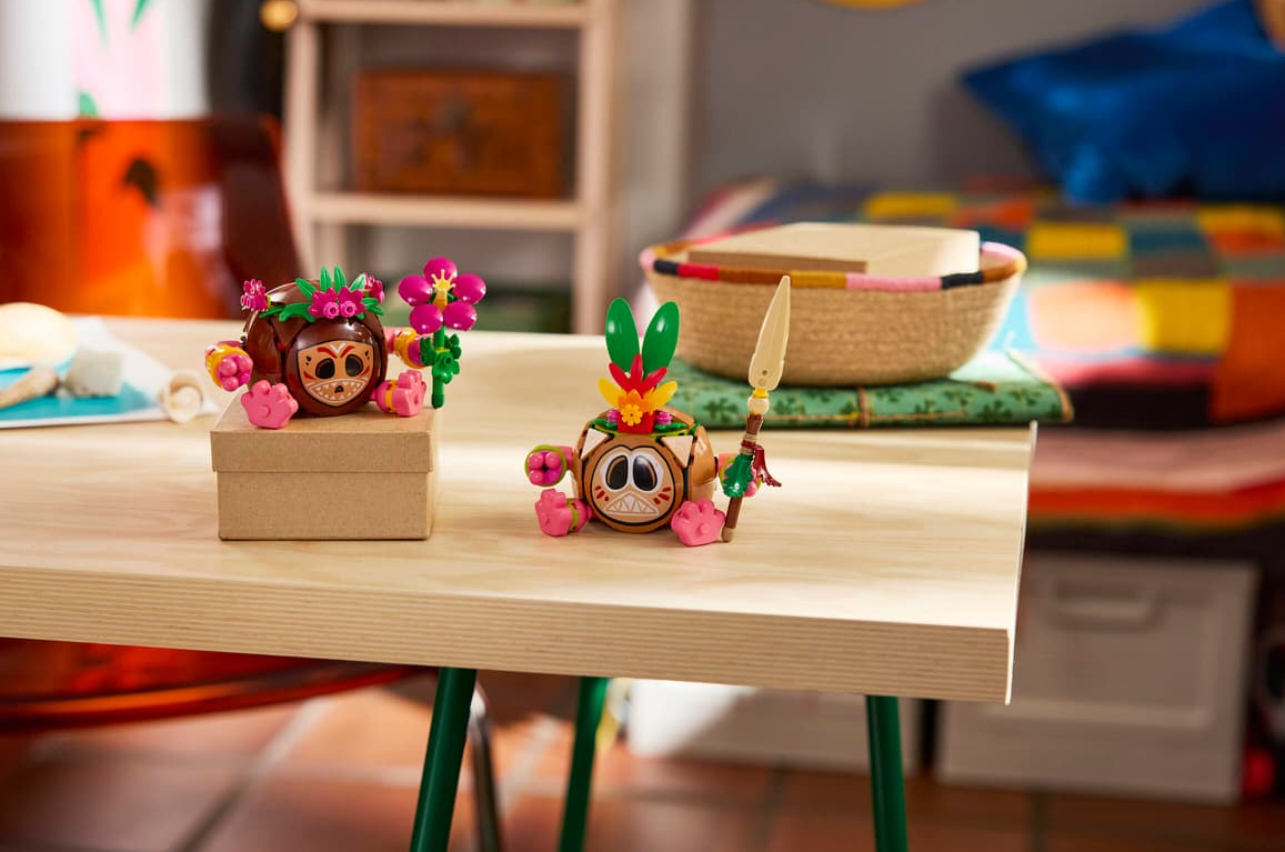 Zwei bunte Spielzeugfiguren mit Blumen und Speer auf einem Holztisch.