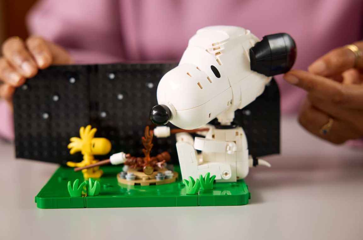 Lego Snoopy und Woodstock mit Lagerfeuer. Hände einer Person ordnen die Szene.