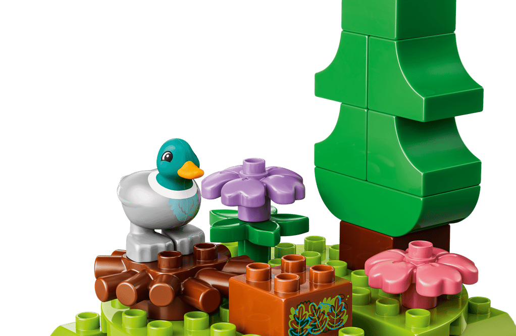 Eine Lego-Ente sitzt neben lila und rosa Blumen neben einem grünen Baum.