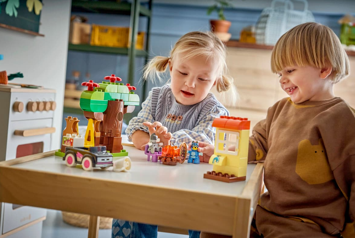 Zwei Kinder spielen mit bunten LEGO-Steinen und bauen ein Baumhaus und Fahrzeug.