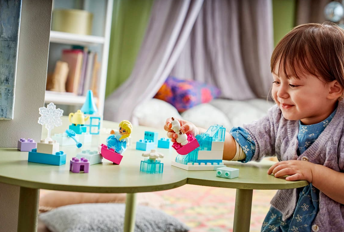 Ein kleines Mädchen spielt mit bunten Lego-Figuren und Bausteinen auf einem Tisch.