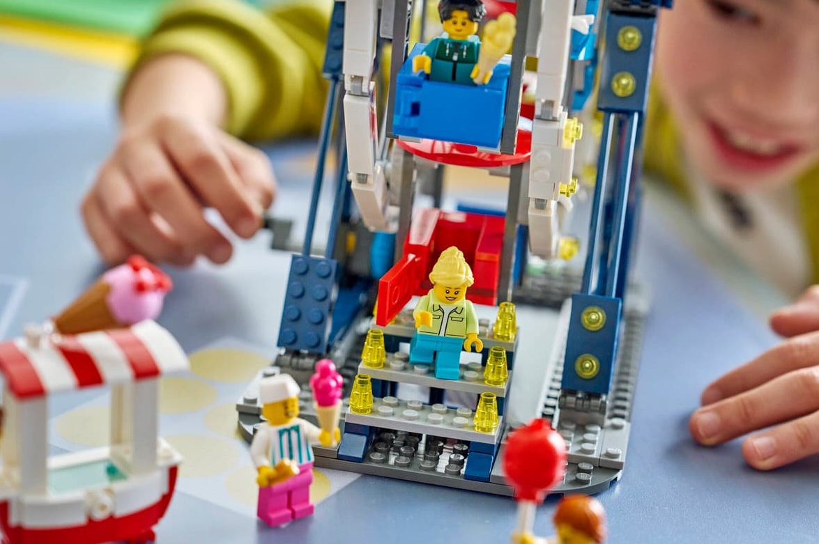 Kind spielt mit einem Lego-Riesenrad, Eisstand und Minifiguren.