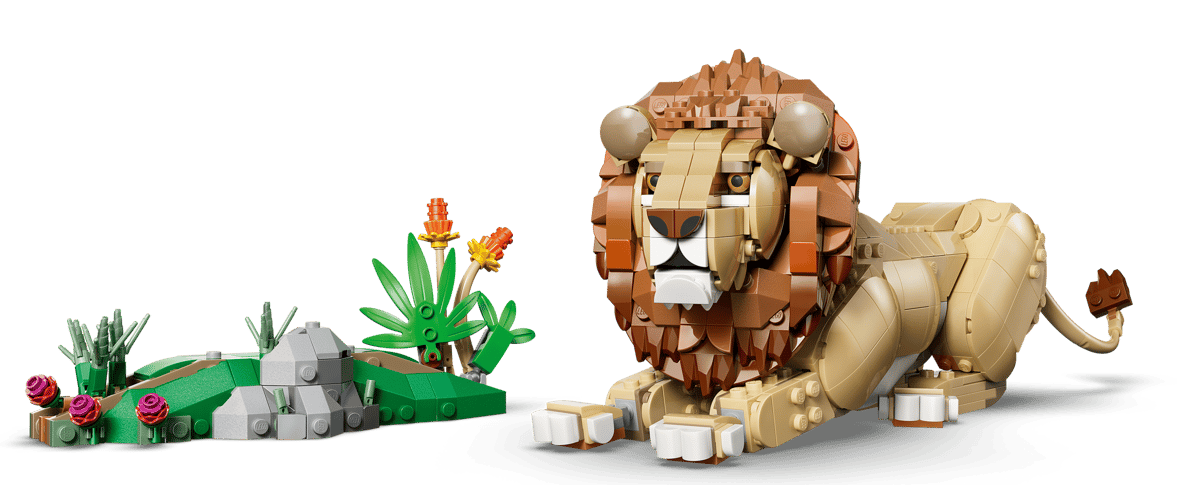 Ein Lego-Löwe liegt neben einem felsigen, grünen Hügel mit Blumen und Pflanzen.