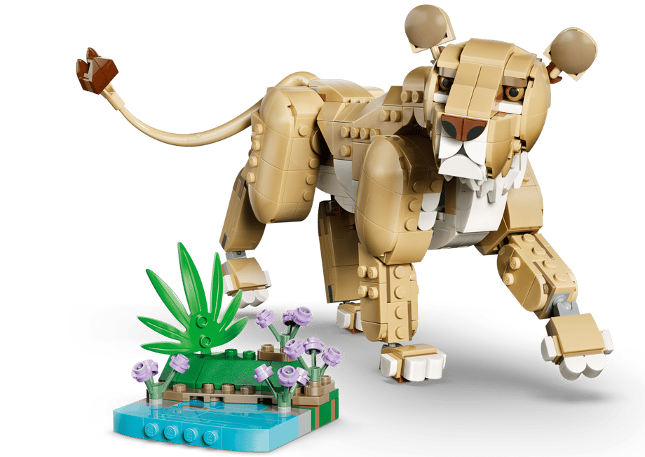 Ein Lego-Löwe mit braunen und weißen Steinen, der auf einem kleinen Diorama mit grünen Blättern und lila Blumen steht.