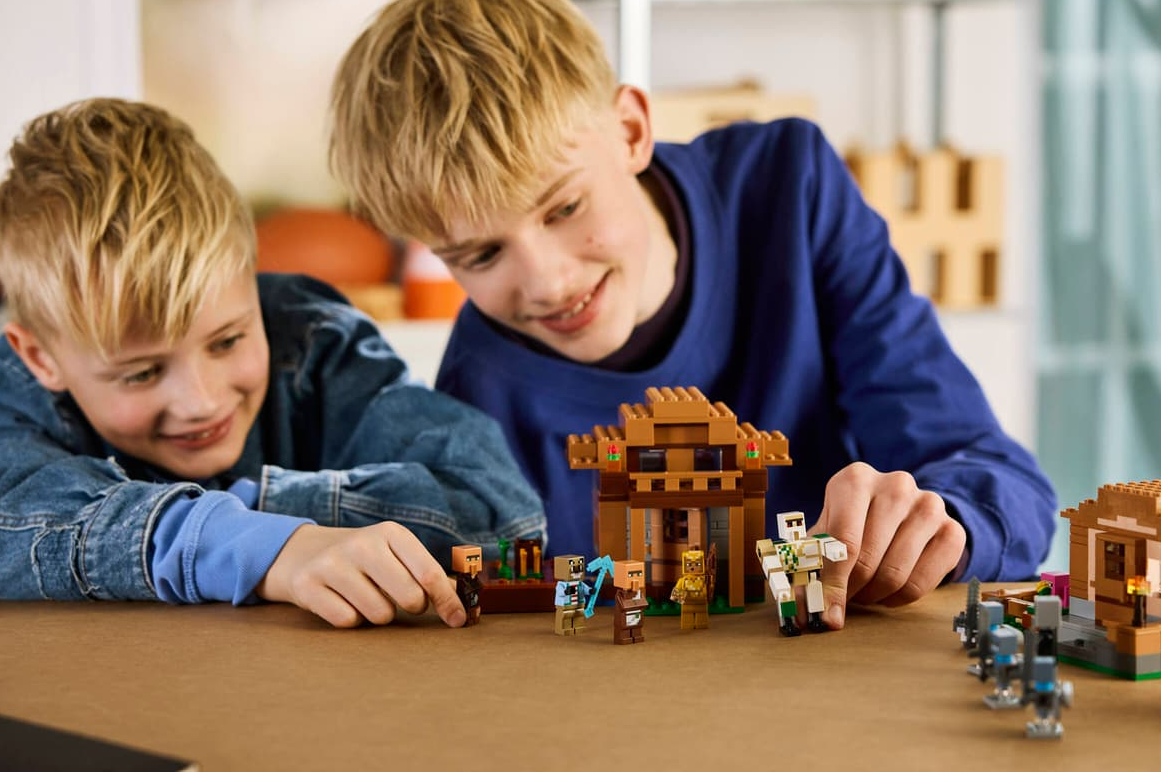 Zwei Jungen bauen Minecraft Lego Sets mit Figuren und Strukturen auf einem Tisch.