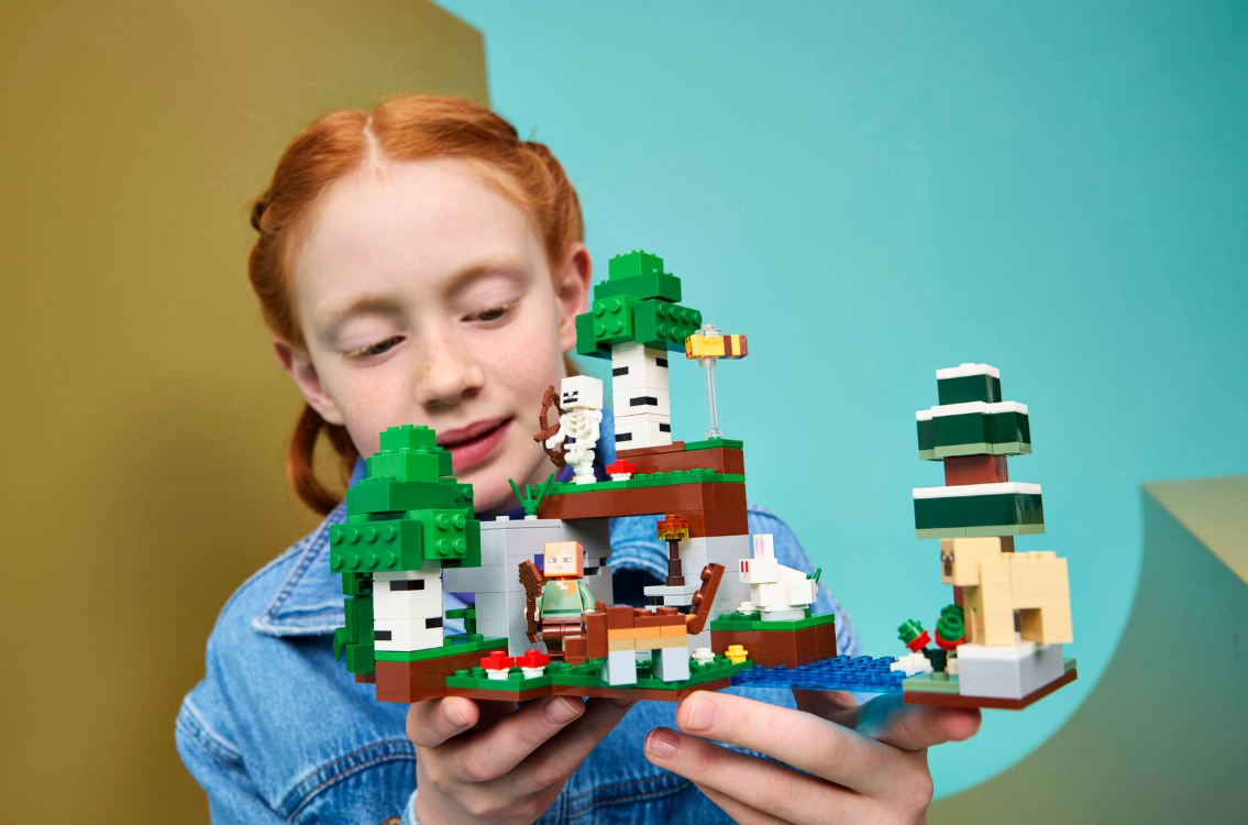 Mädchen hält Minecraft LEGO Set mit Steve, Skelett, Wolf, Hase und Bäumen.