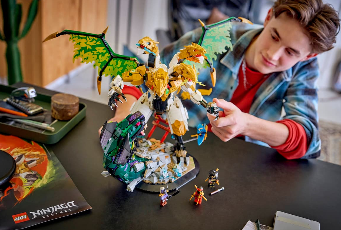 Ein Junge baut einen Lego-Drachen mit grünen Flügeln und mehreren Köpfen, mit Minifiguren drumherum.