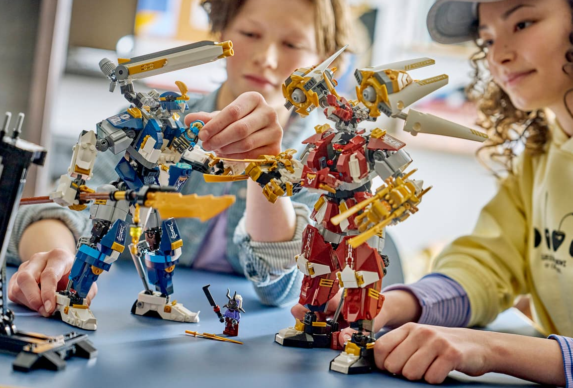 Zwei Kinder bauen und spielen mit roten und blauen Lego-Robotern auf einem Tisch.