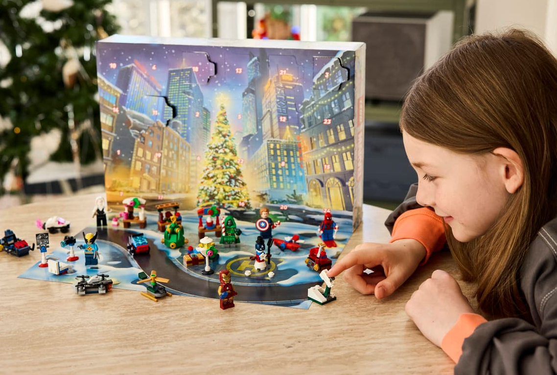 Mädchen schaut auf Lego-Adventskalender mit Marvel-Figuren und Weihnachtsszene.