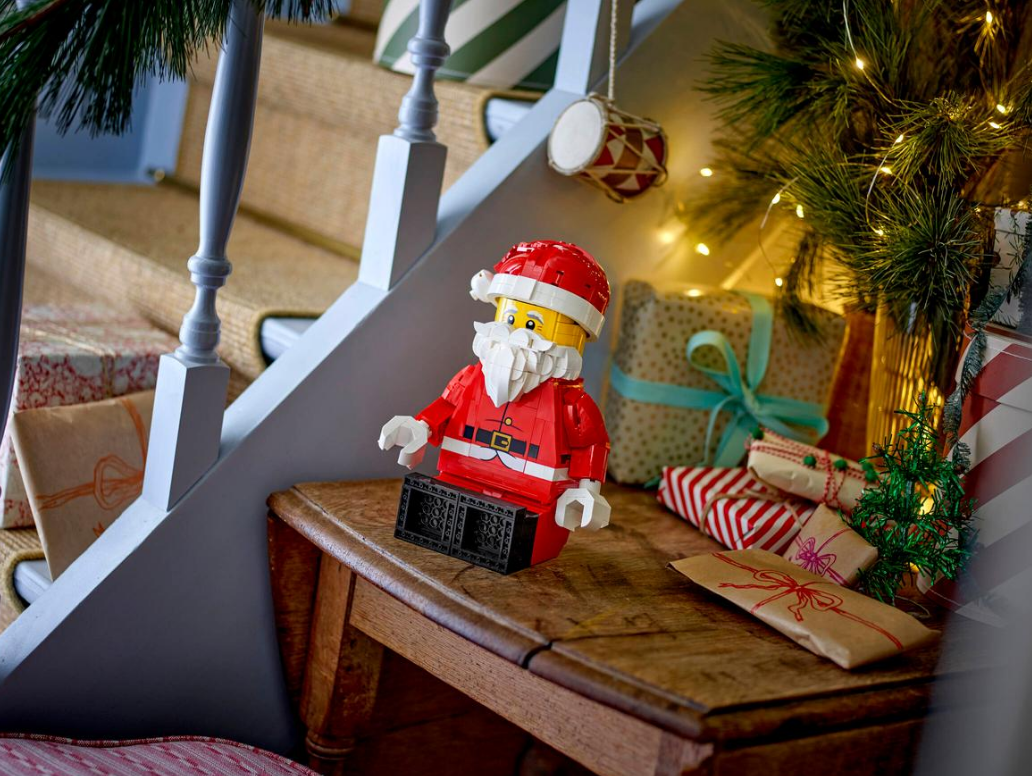 Ein Lego-Weihnachtsmann sitzt neben Weihnachtsgeschenken auf einem Holztisch.