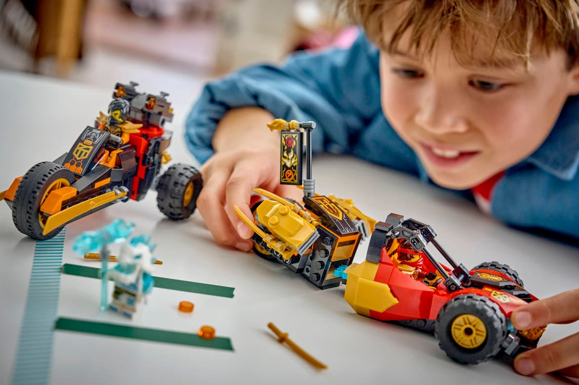Ein Junge spielt mit roten, gelben und schwarzen Lego-Fahrzeugen und Figuren auf weißer Oberfläche.
