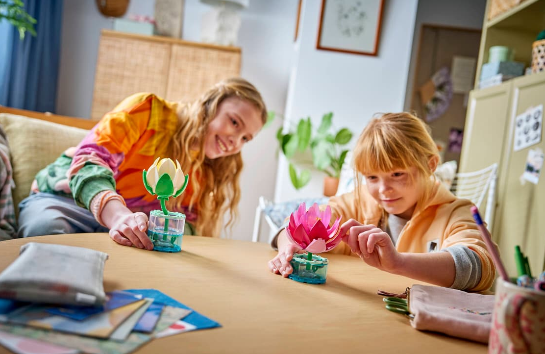 Zwei Mädchen bauen Blumen aus Legosteinen an einem Holztisch.