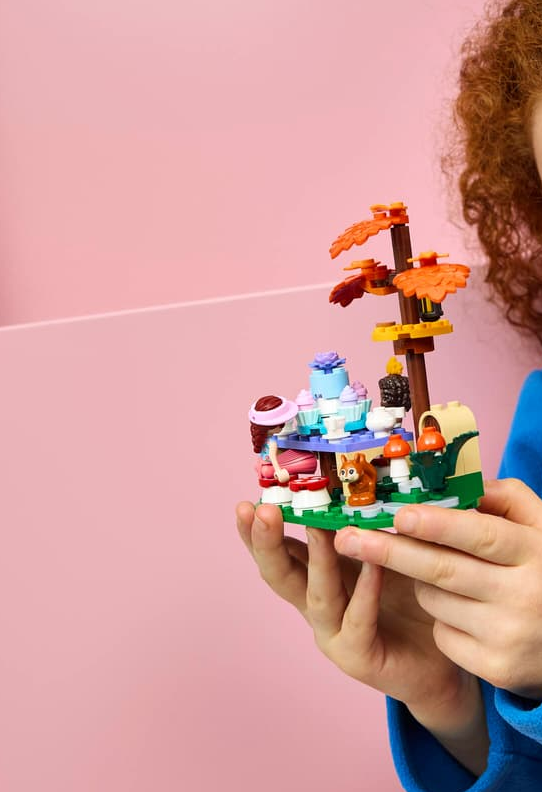Hände halten ein Lego-Modell mit einem Kuchen, einer Figur und einem Eichhörnchen.