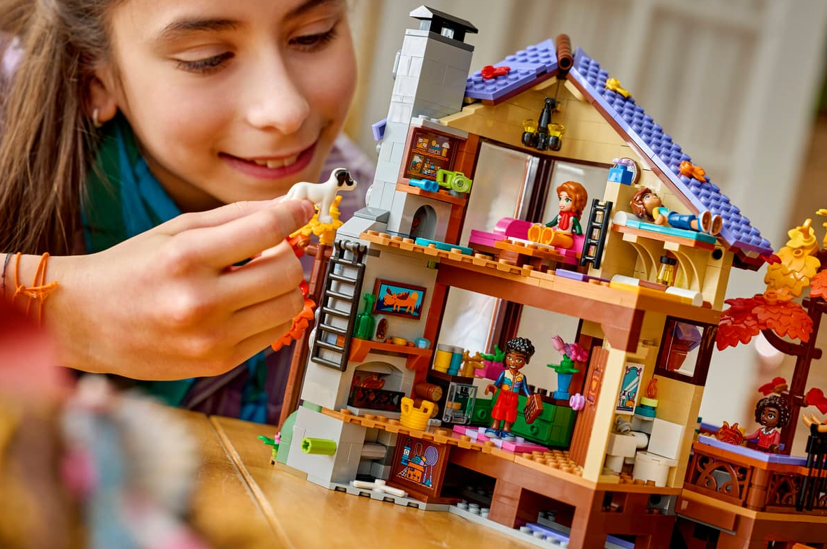 Mädchen spielt mit einem mehrstöckigen Lego-Haus mit Figuren und Zubehör.