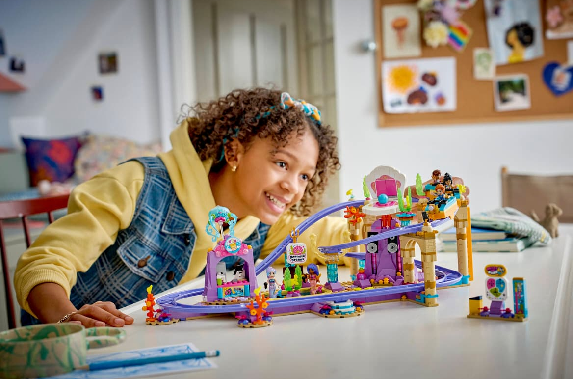 Ein Mädchen spielt mit einem bunten Lego-Achterbahn-Spielzeug auf einem Tisch.