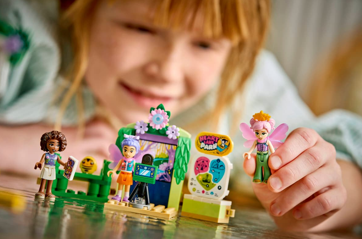 Mädchen spielt mit Lego-Figuren vor einer Kulisse mit Kamera und Schmetterlingen.