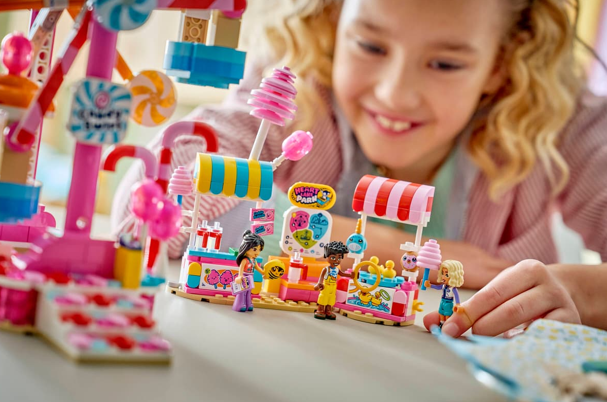 Mädchen spielt mit einem bunten Lego-Freizeitpark-Set mit Süßigkeitenständen und Fahrgeschäften.