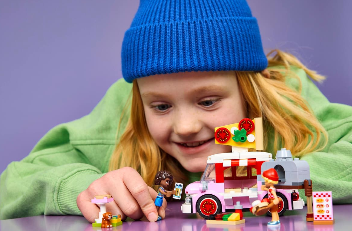 Ein Mädchen spielt mit Lego-Figuren, einem rosa Foodtruck und einem Ofen.