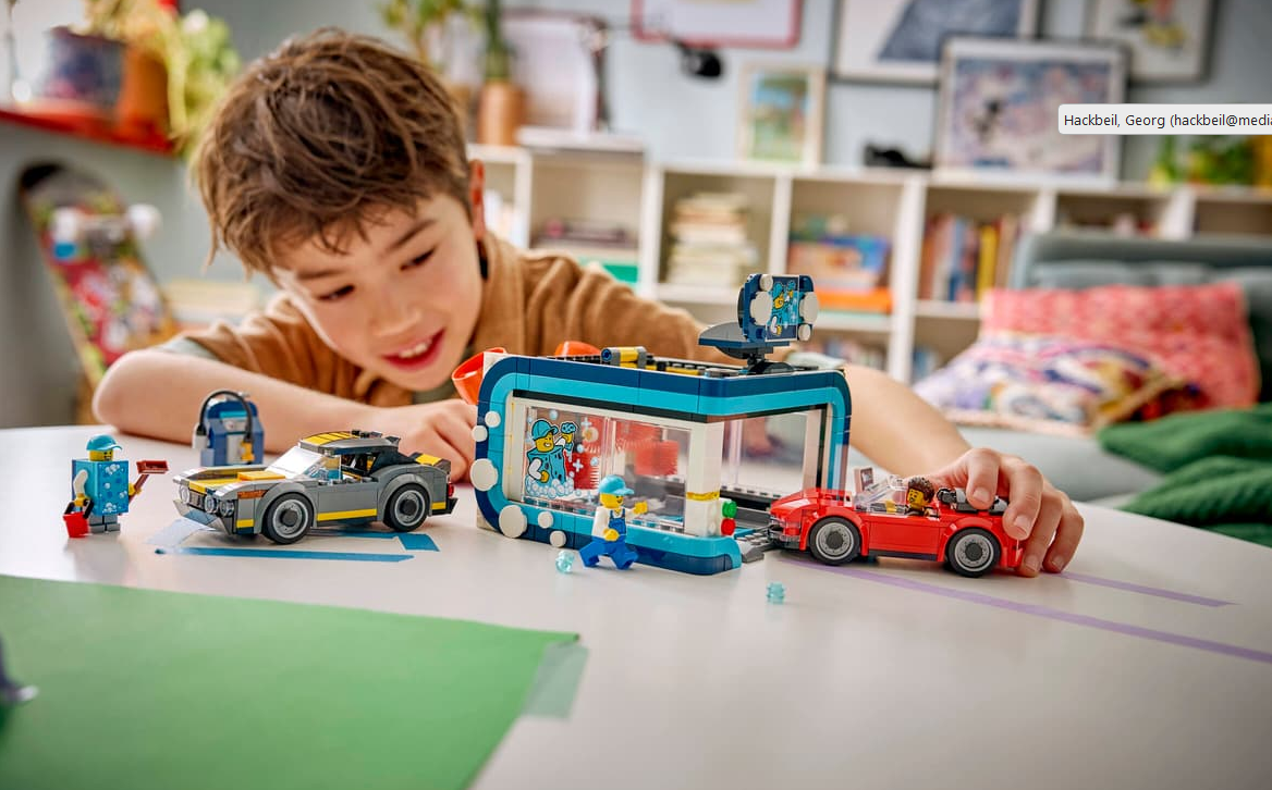 Ein Junge spielt mit Lego-Autos und einer Tankstelle auf einem Tisch.