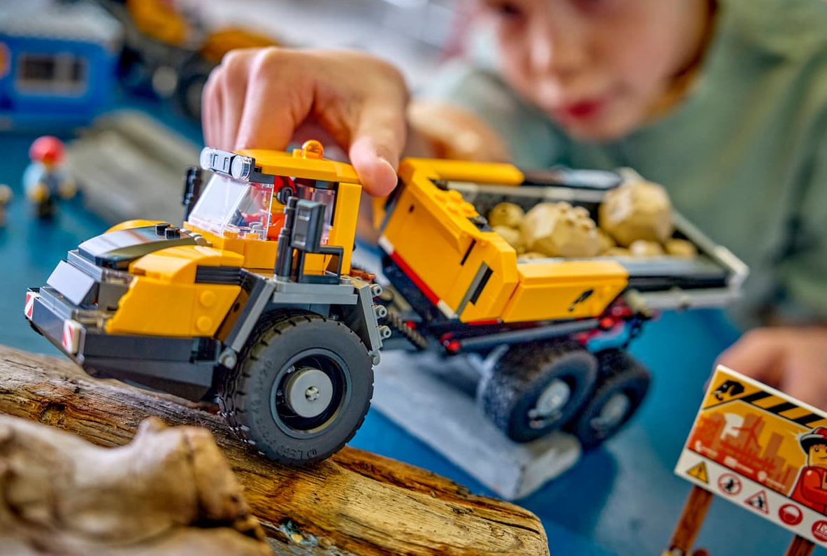 Ein gelber Lego-Kipper mit Steinen wird von einer Hand gehalten. Nahaufnahme.