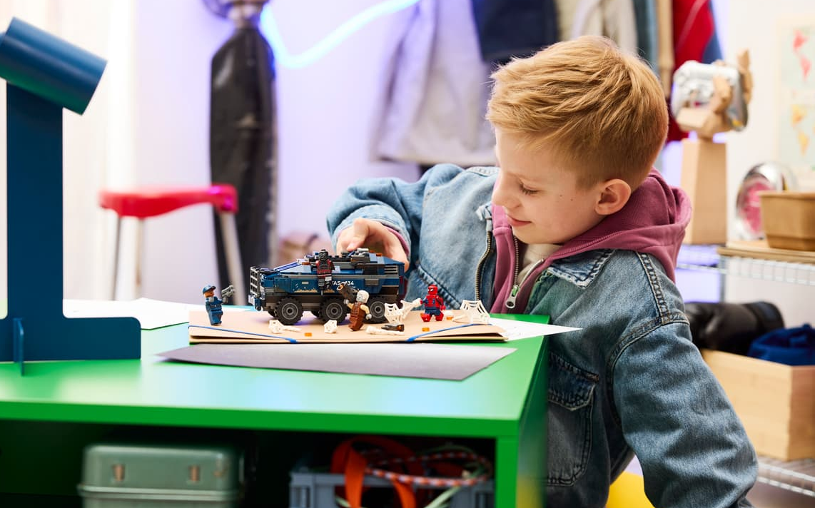 Ein Junge spielt mit Lego-Figuren und einem Spielzeugauto auf einem grünen Tisch.