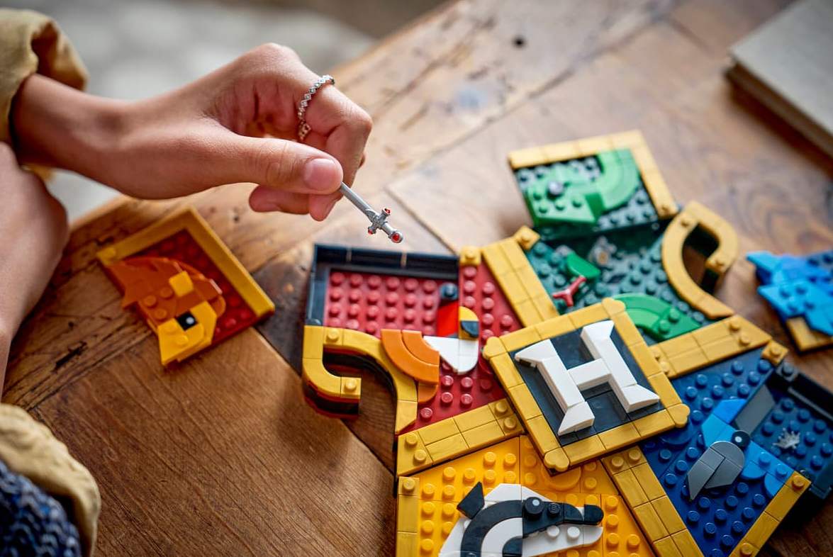 Eine Hand hält ein kleines Schwert über einem Lego-Brett mit verschiedenen Hogwarts-Häusern.