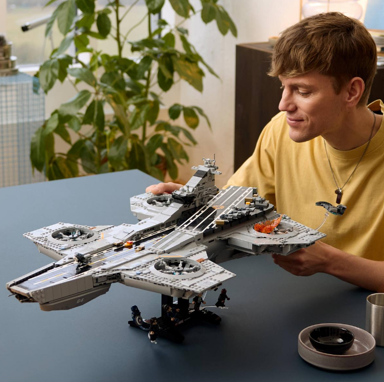 Mann hält Lego-Nachbildung eines grauen Raumschiffs mit orangefarbenen Flammen.