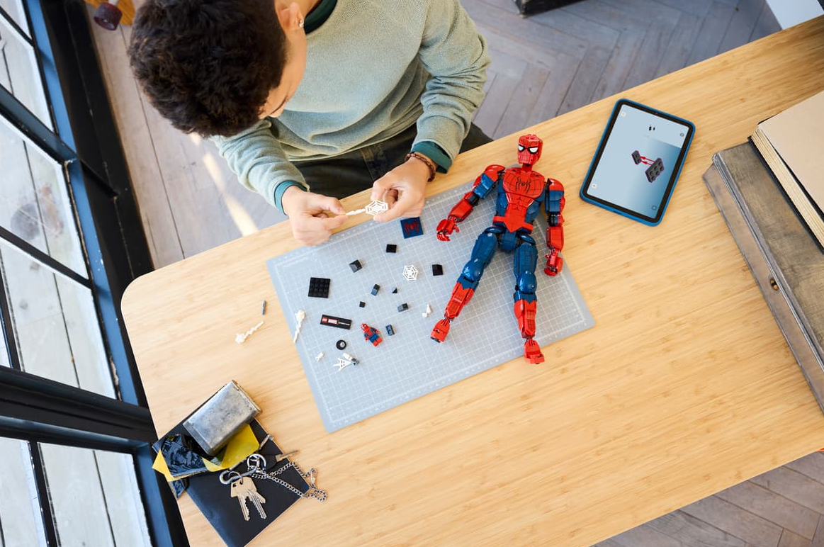 Eine Person baut eine Spiderman-Figur mit Legosteinen auf einem Tisch.