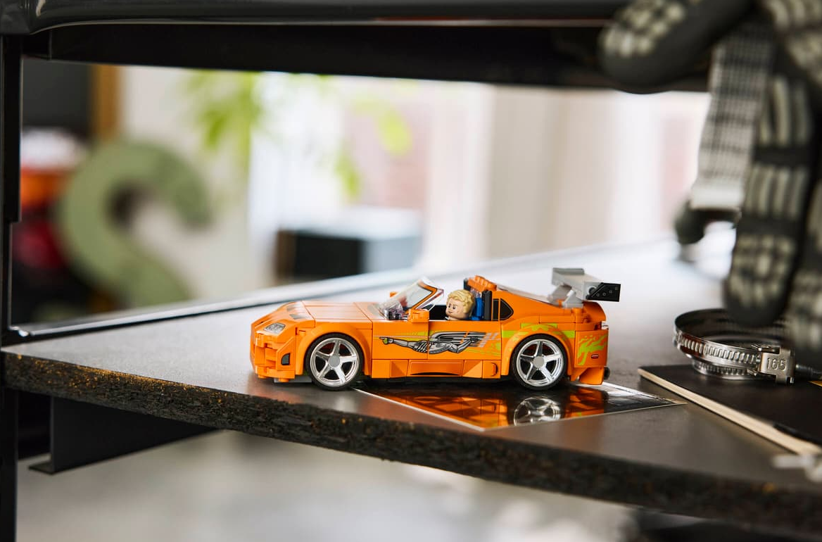 Orange Lego Auto mit Fahrerfigur auf einem Regal.