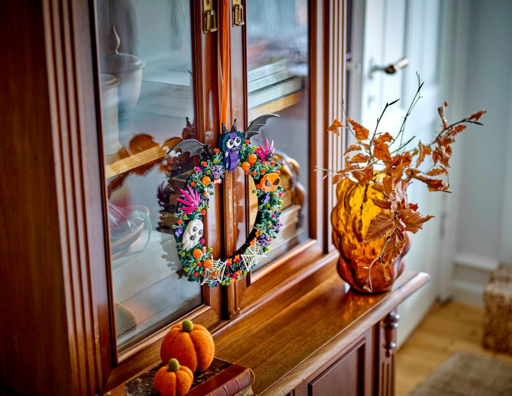 Halloween-Kranz mit Eule, Fledermaus, Kürbissen und Geistern hängt an einem Holzschrank.