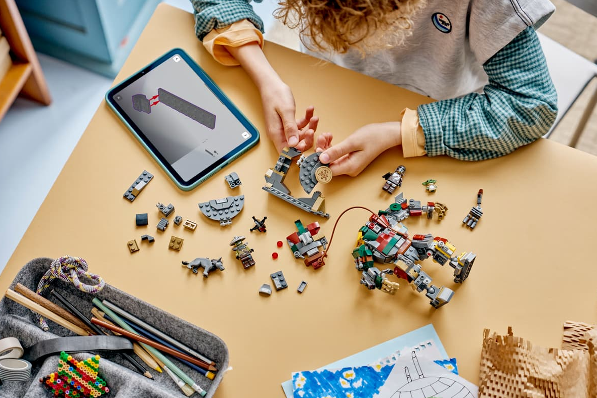 Ein Kind baut ein Lego-Set mit einem Tablet als Anleitung. Teile liegen verstreut.
