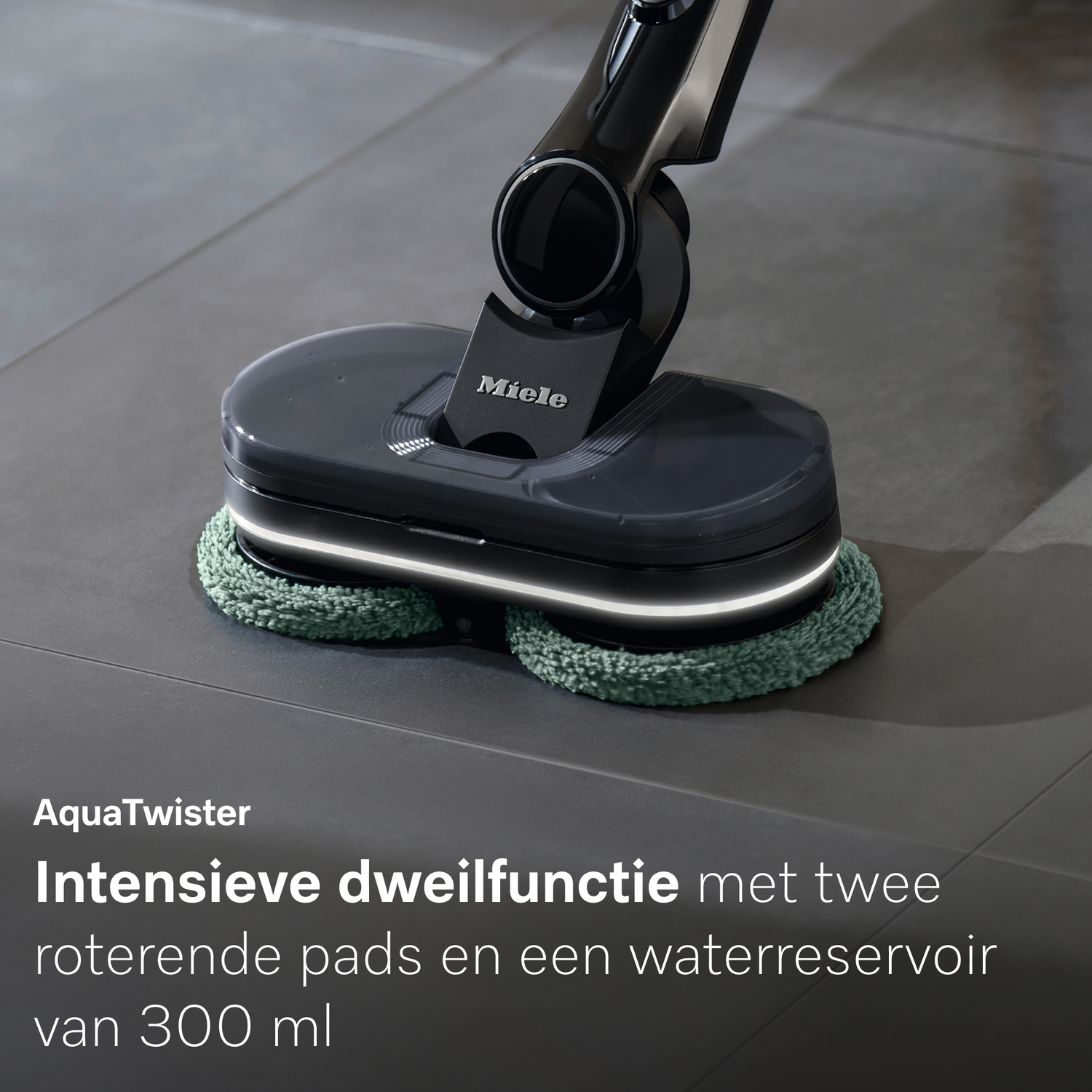 Een Miele vloerreiniger met roterende pads op een grijze tegelvloer.