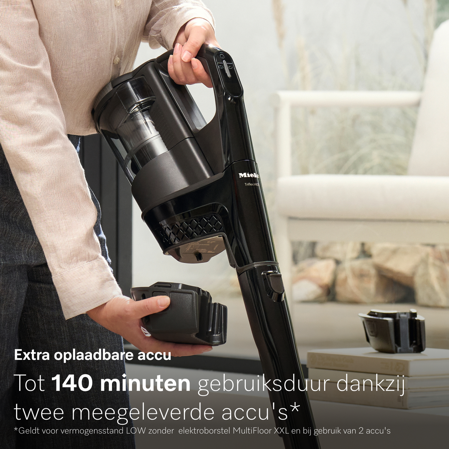 Een persoon houdt een zwarte Miele steelstofzuiger met afneembare accu vast.