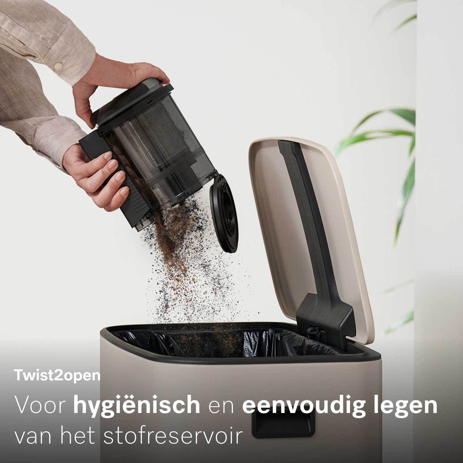 Een man leegt een stofreservoir in een prullenbak. Stof valt eruit.