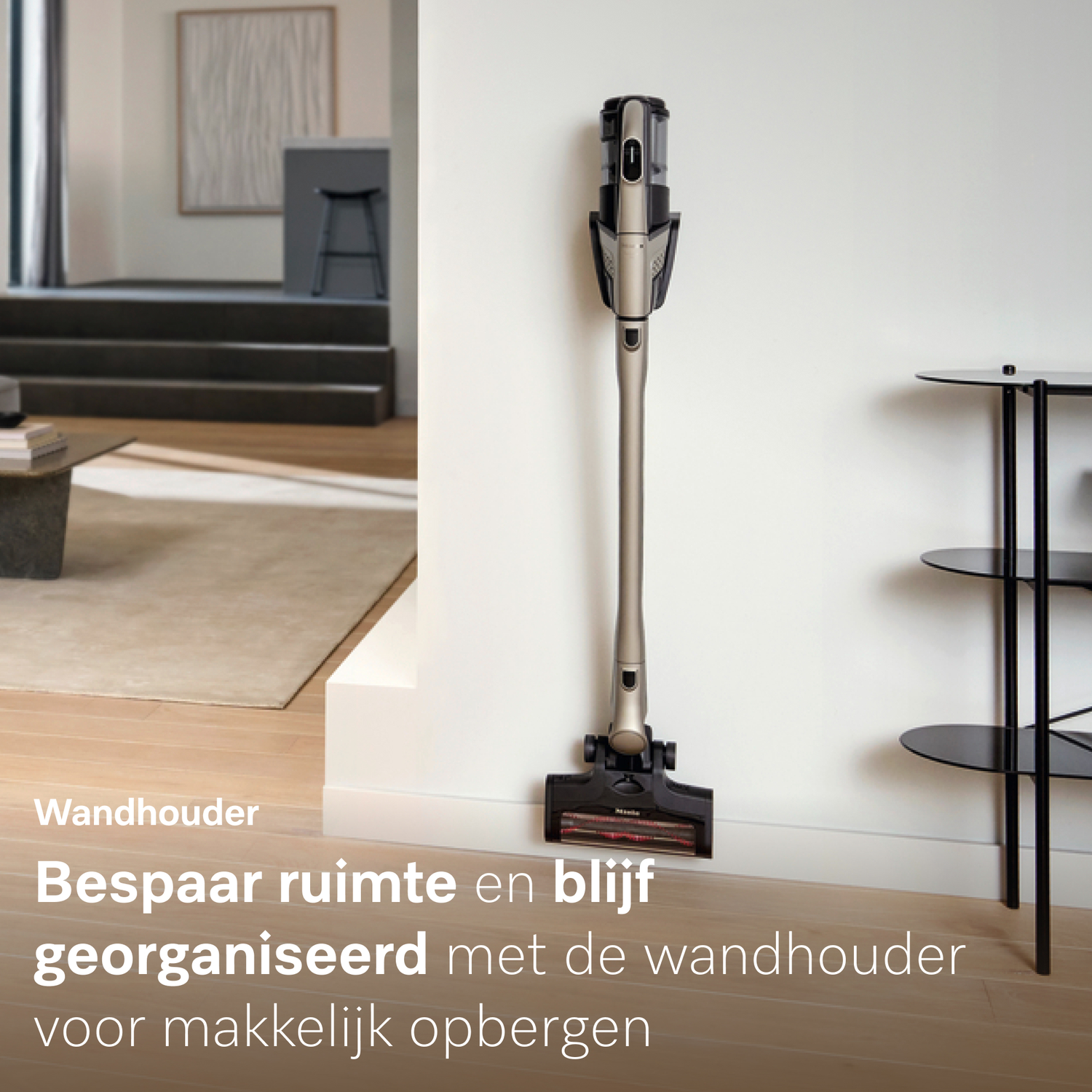Een draadloze stofzuiger is aan een witte muur bevestigd, naast een bijzettafel.