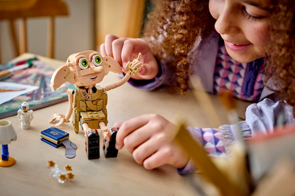 Ein Mädchen baut mit Lego, Dobby sitzt daneben, mit einem Buch und Socken.