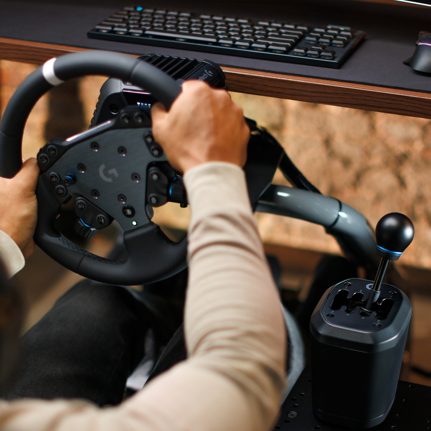 Manos en un volante y palanca de cambios de gaming, con teclado y ratón al fondo.