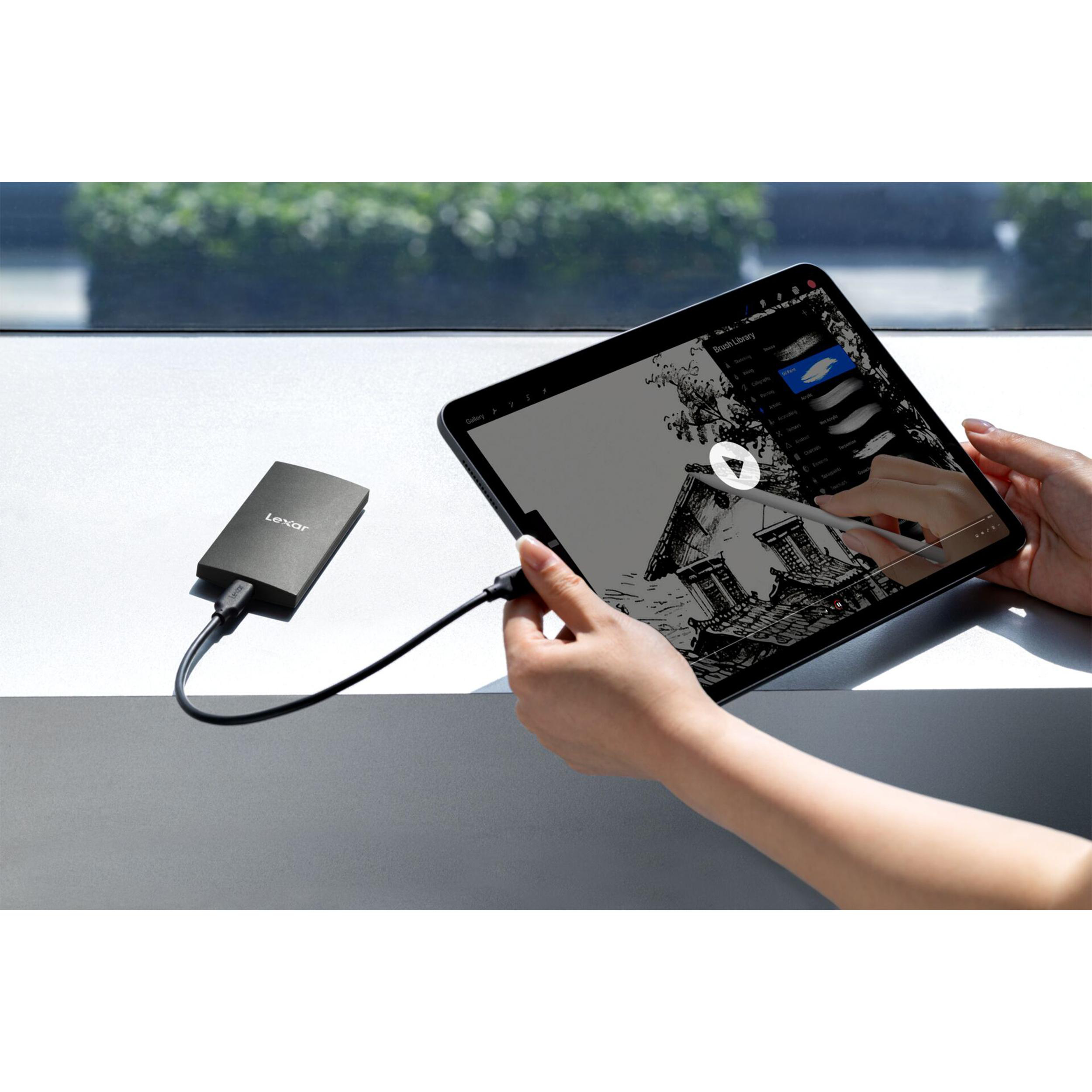 Eine Hand hält ein Tablet, das mit einer externen Festplatte verbunden ist. Zeichen-App geöffnet.