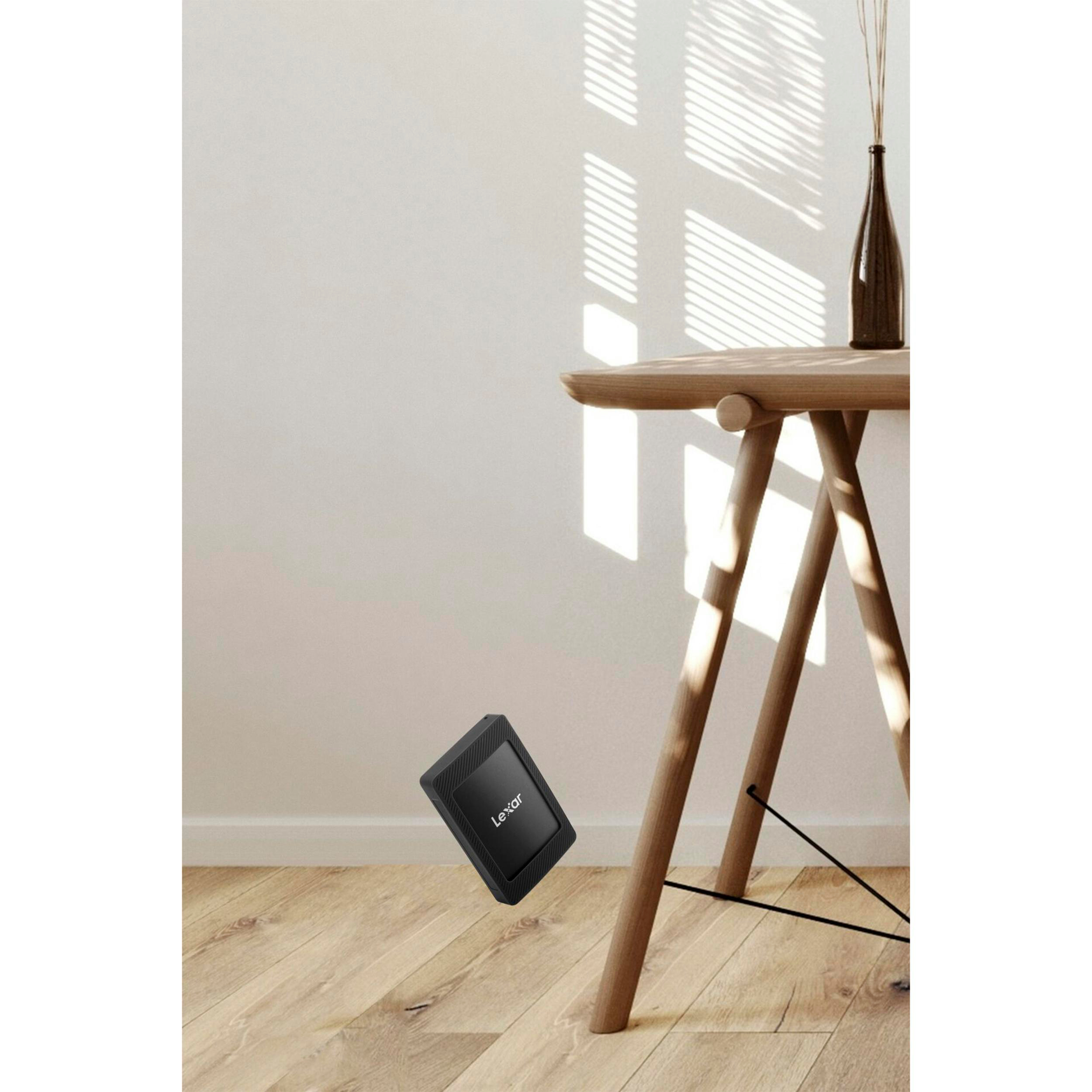 Schwarzer Lexar SSD auf Holzboden neben einem Tisch mit Vase.