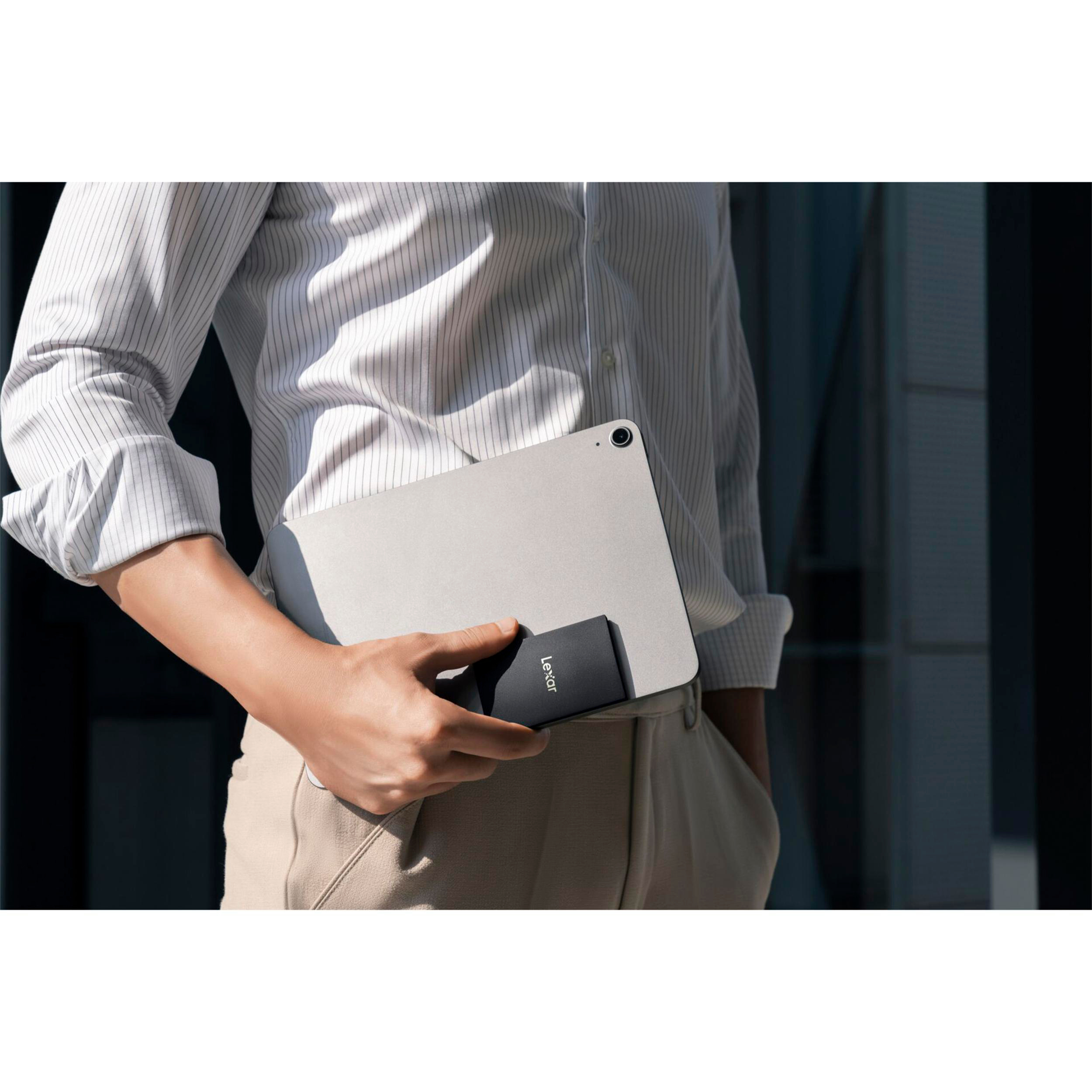 Person hält eine schwarze externe SSD neben einem Tablet.