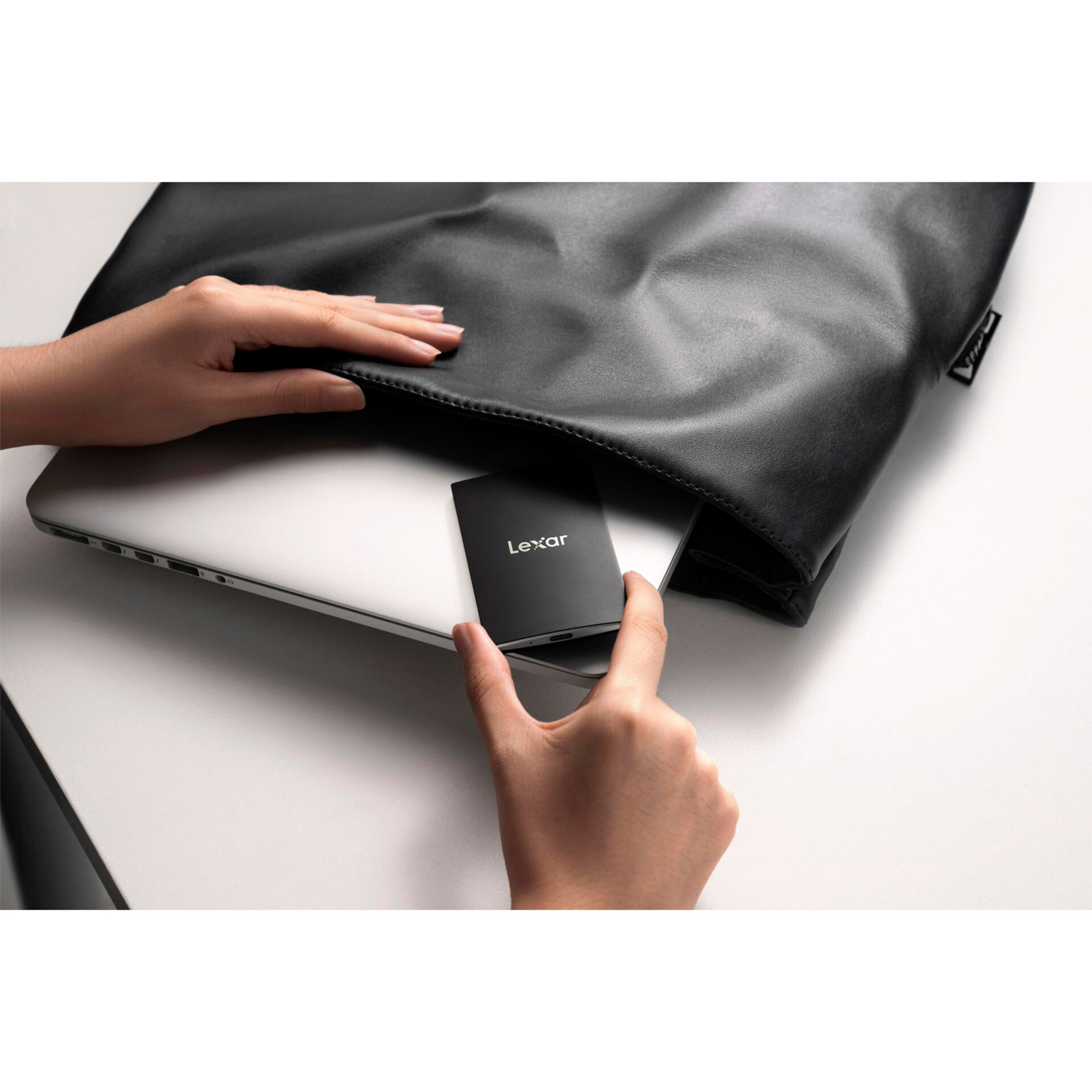Eine Hand legt eine schwarze Lexar-Festplatte neben einen Laptop in eine Tasche.