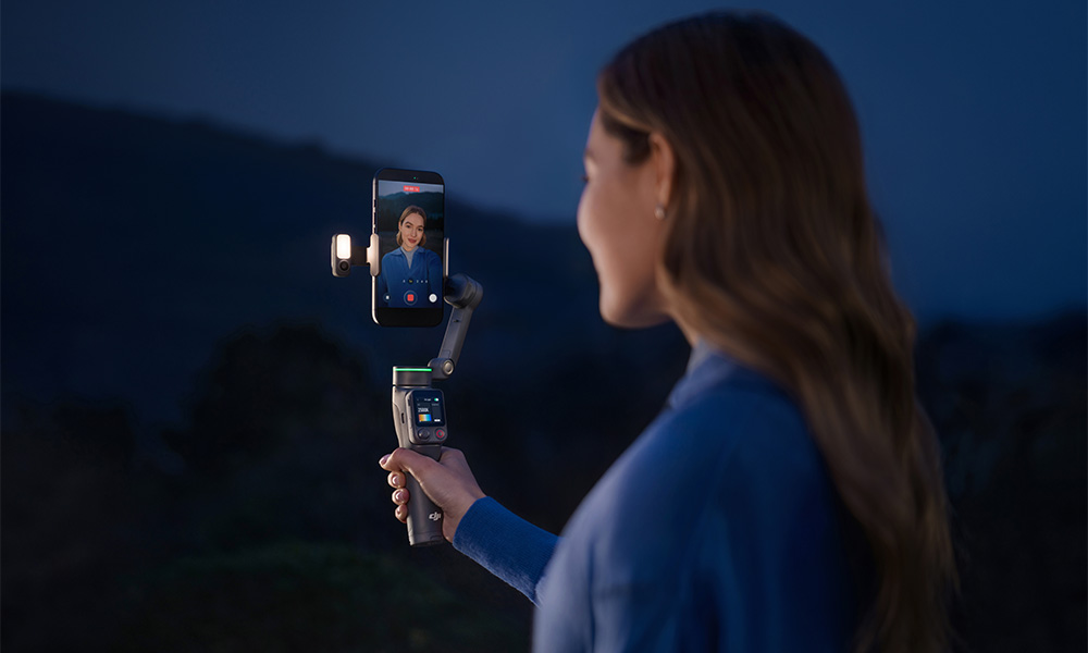 Kobieta trzyma gimbal z telefonem w nocy, światło się świeci.