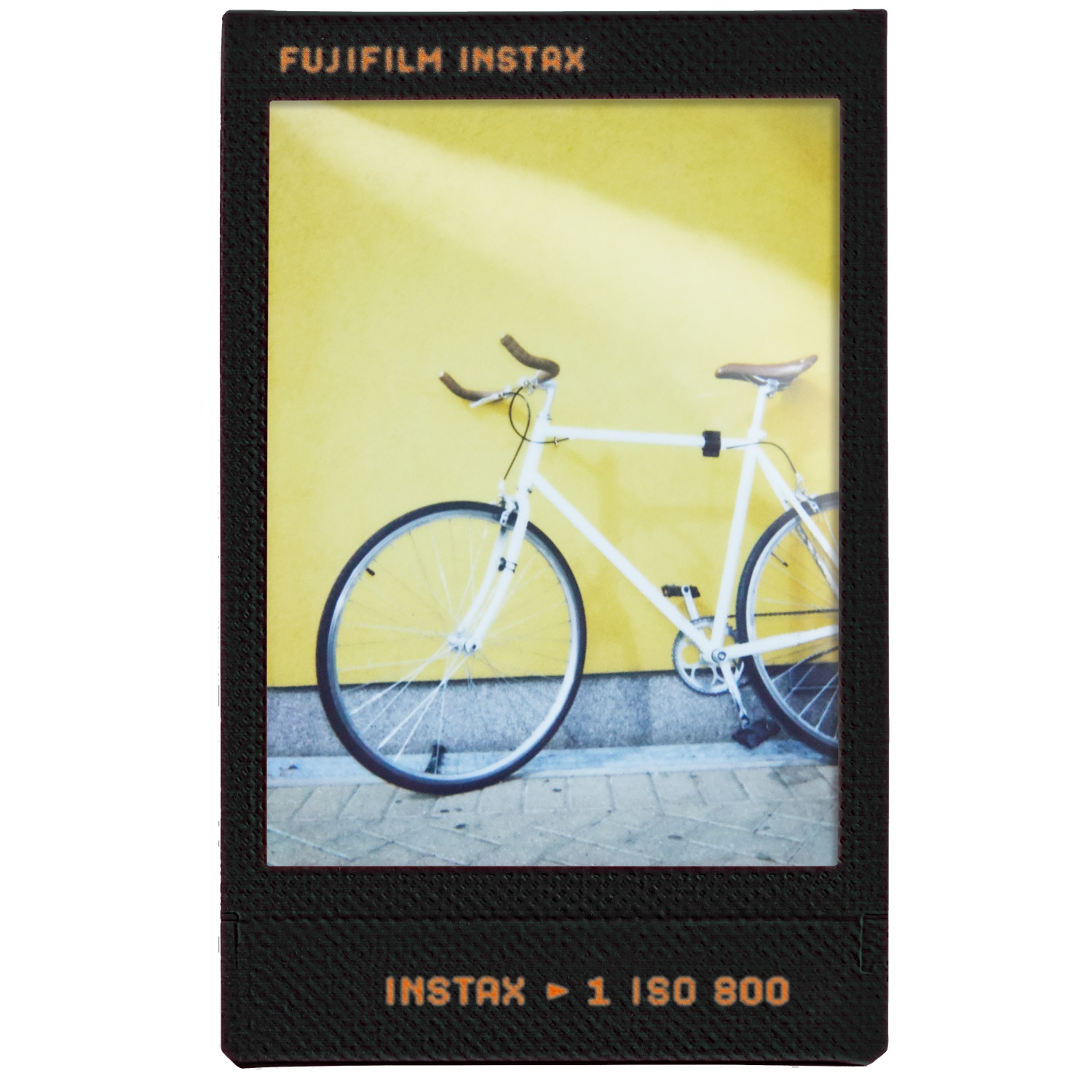 Een witte fiets staat tegen een gele muur op een betegeld trottoir.
