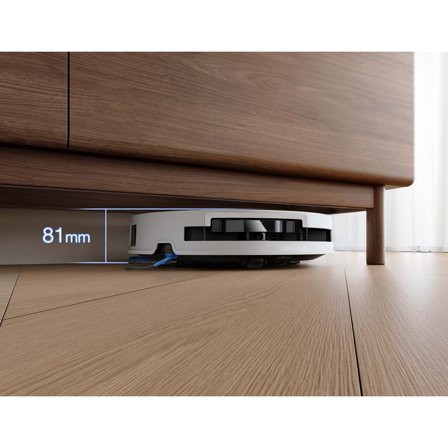 Un robot aspirapolvere bianco pulisce sotto un mobile in legno. Indicata l'altezza di 81 mm.