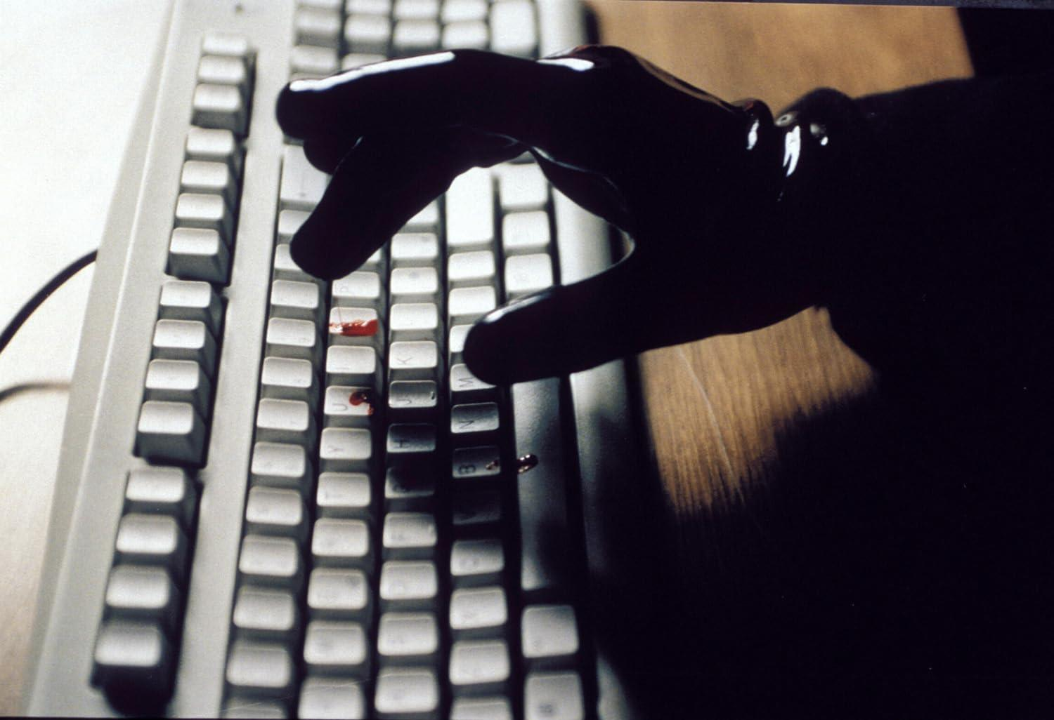 Eine behandschuhte Hand berührt eine Tastatur mit Bluttropfen.