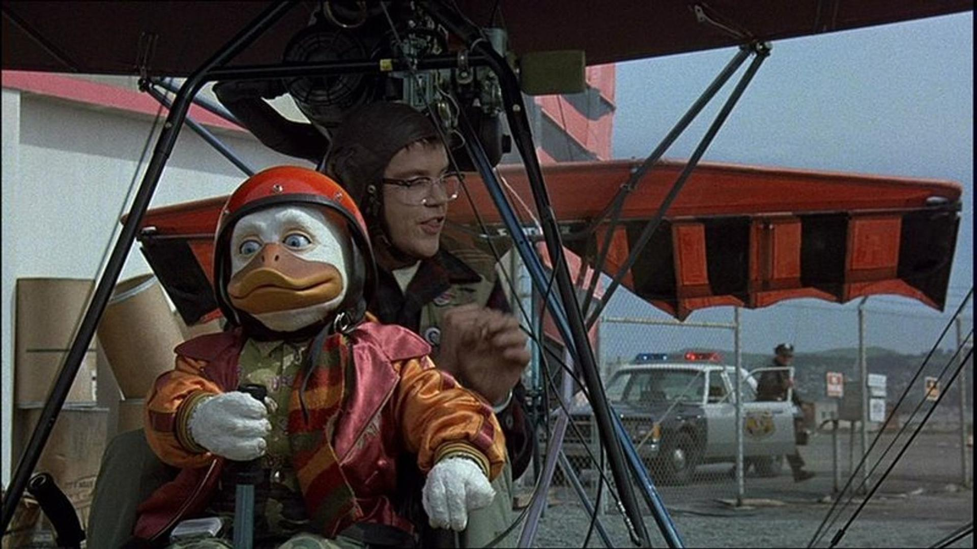 Eine anthropomorphe Ente mit Helm und Pilot hinter ihr in einem Flugzeug.