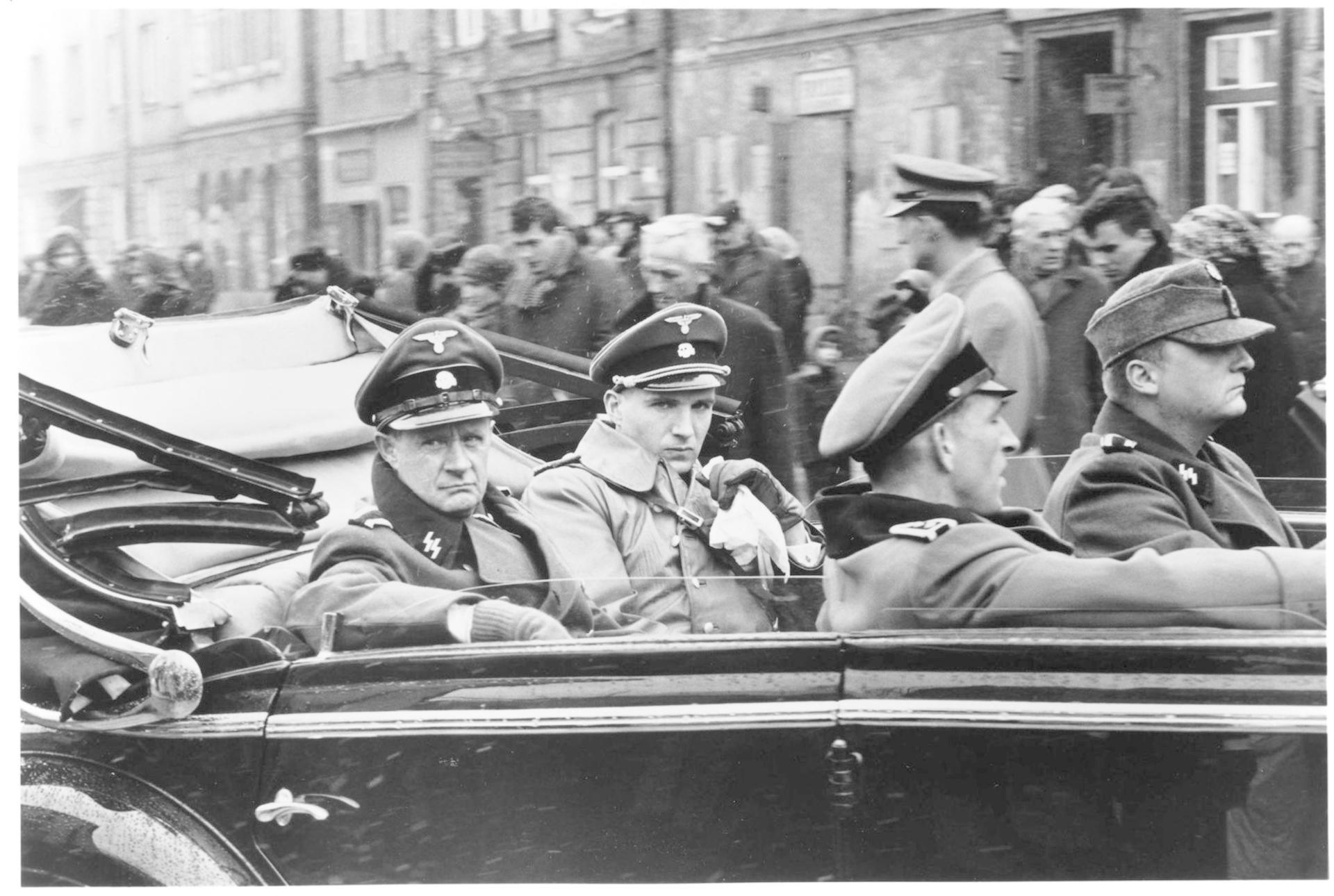 Männer in Uniform sitzen in einem offenen Auto, Menschenmenge im Hintergrund.