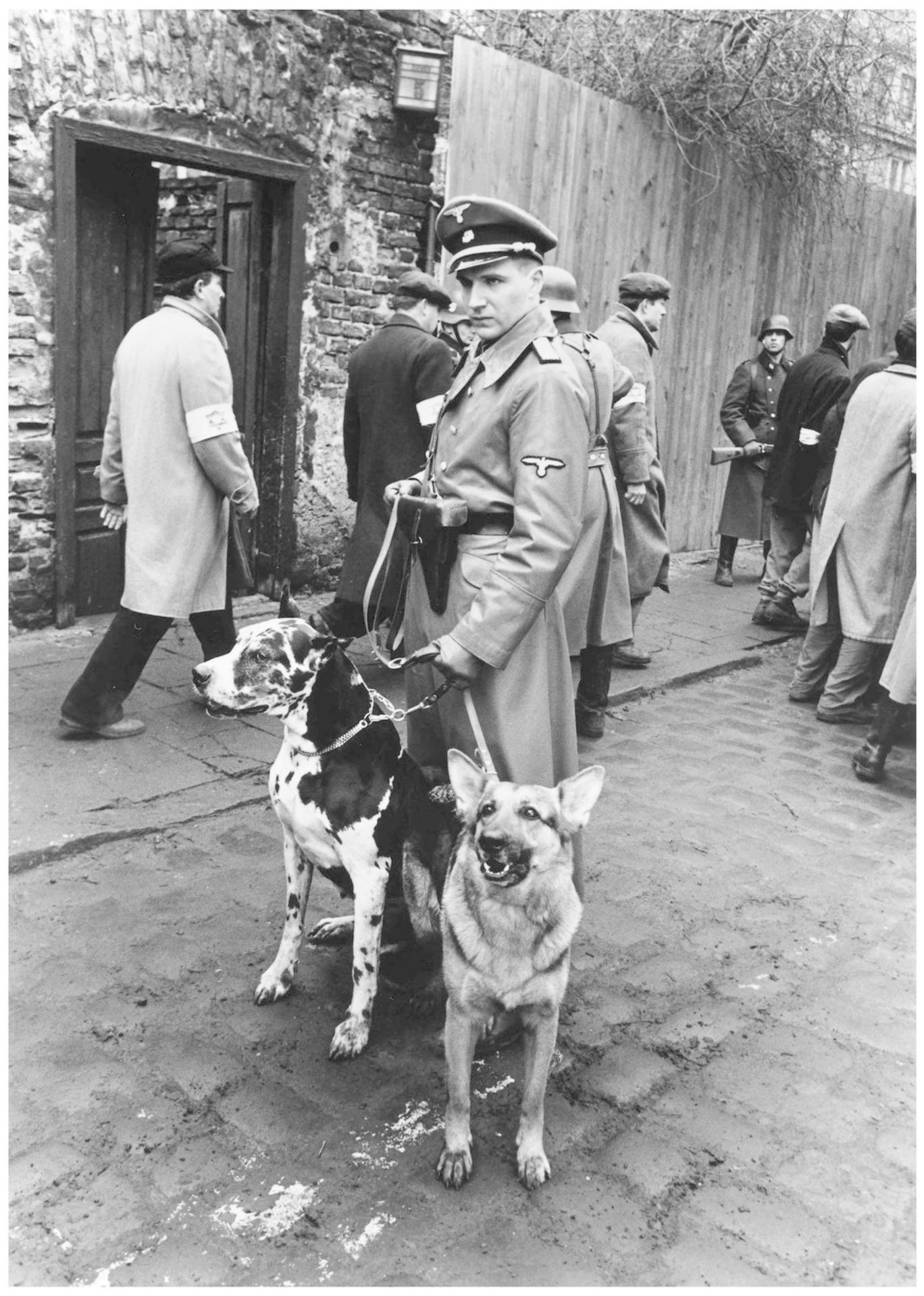 Männer in Uniform mit Hunden auf einem Hof. Ein Mann hält zwei Leinen.