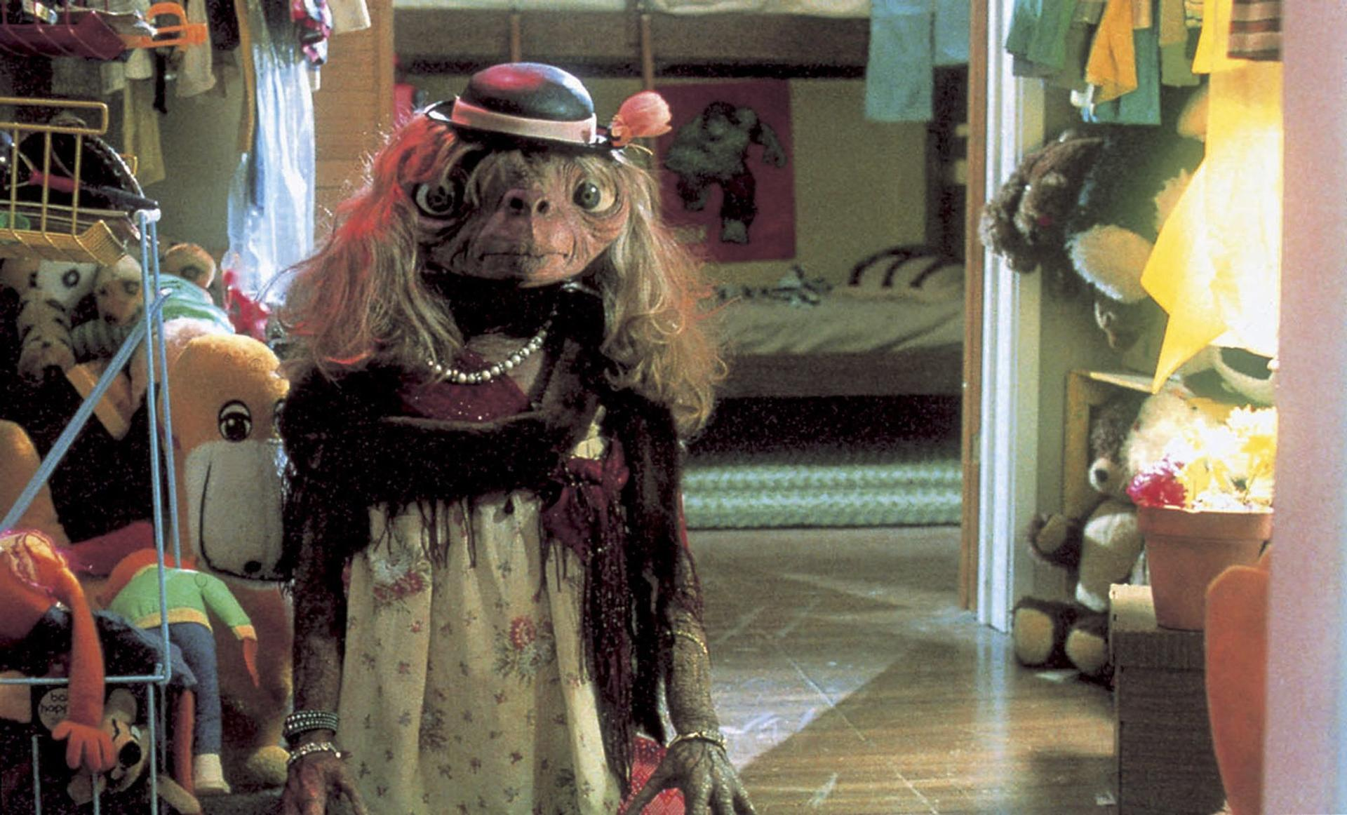 E.T. trägt eine Perlenkette, einen Hut und ein Kleid im Zimmer.